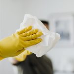 Close-up of a yellow-gloved hand cleaning a mirror with a cloth indoors.